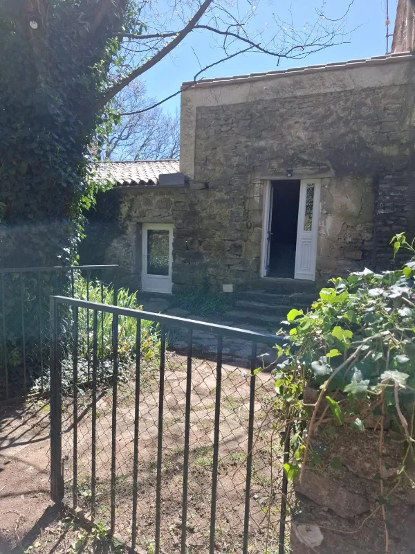 Façade en pierre du Mas de Gréfeuille avec son portail d'entrée dans un écrin de verdure