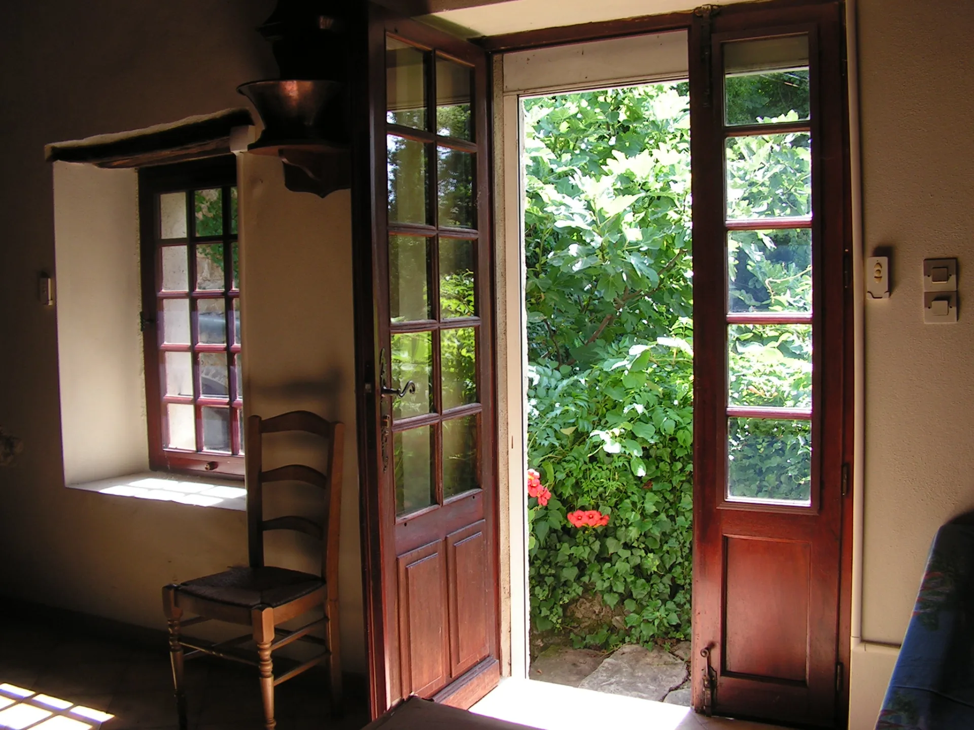 Entrée du mas avec porte-fenêtre en bois ouverte sur le jardin verdoyant