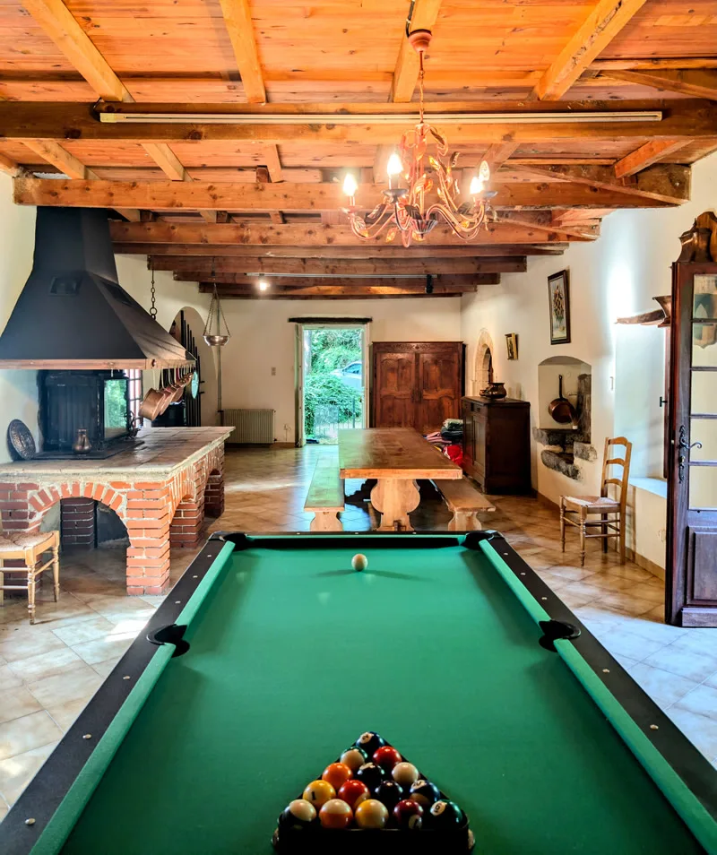Grand salon avec billard, poutres apparentes et cheminée en pierre
