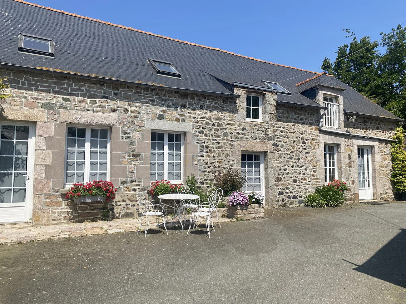 Gîte de groupe Le Grand Gîte de Bel Hêtre à Saint-Alban — Façade en pierre de la longère avec jardin fleuri et ciel bleu, capacité 15 personnes