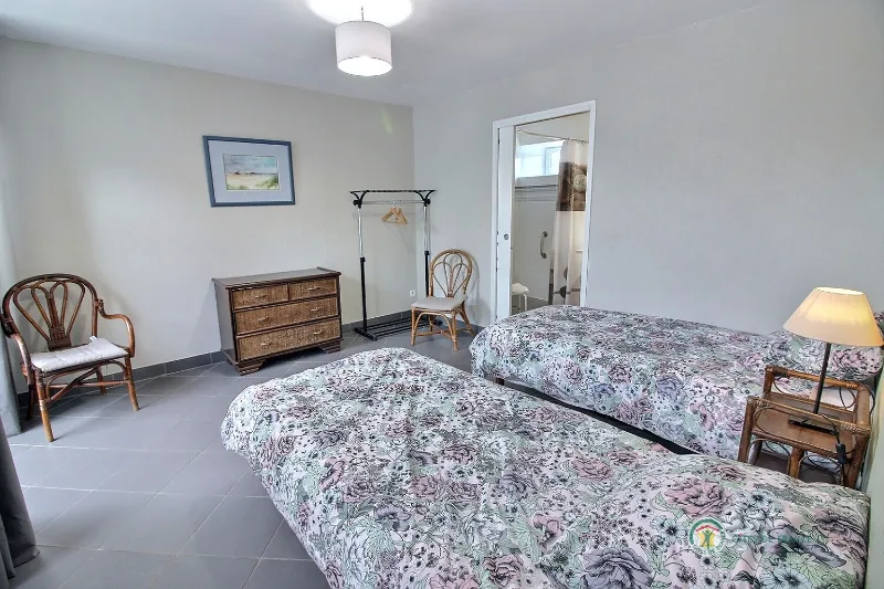 Chambre lumineuse avec deux lits fleuris sous charpente apparente