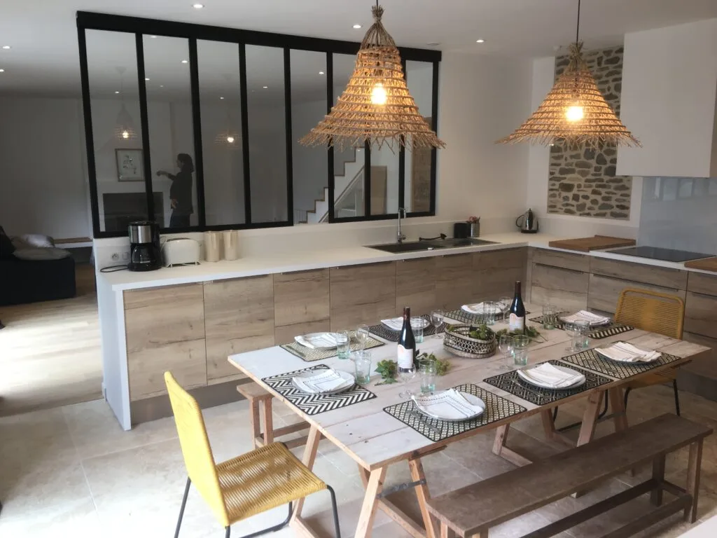 Cuisine équipée ouverte sur une grande table à manger en bois pour douze convives
