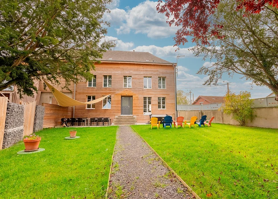 Vue d'ensemble de la maison avec jardin et chaises colorées face à la pelouse