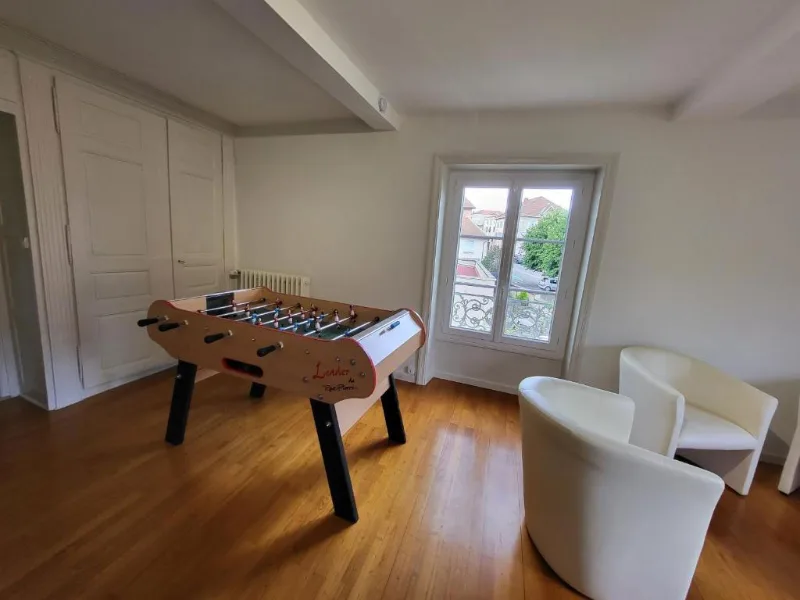 Salle de jeux avec baby-foot et fauteuils sous charpente en bois