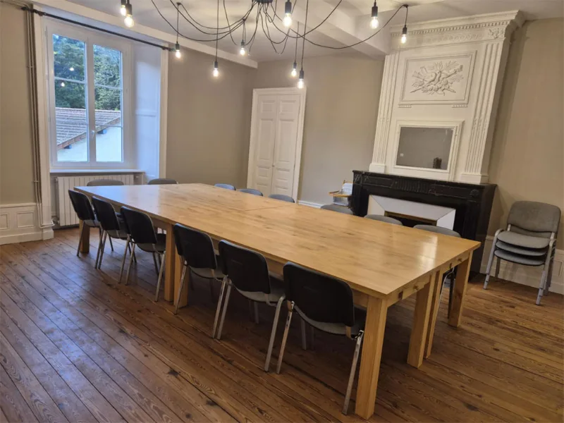 Grande salle à manger avec longue table en bois et seize chaises pour les groupes
