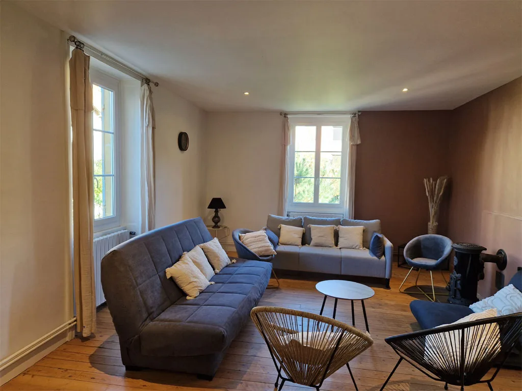 Salon lumineux avec canapés, fauteuils et grandes fenêtres à petits carreaux