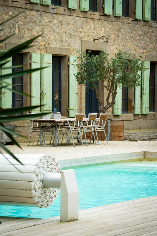 Piscine privative entourée de transats en bois face à la façade en pierre