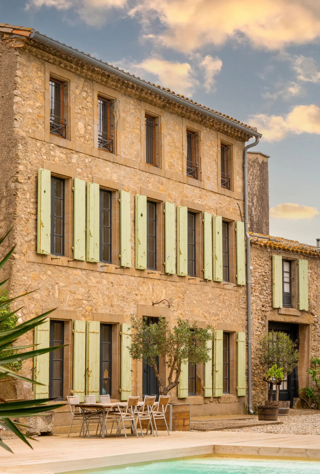 Gîte de groupe Prieuré Saint-Louis à Floure — Façade en pierre de la bastide sur trois niveaux avec volets verts, au cœur du village de Floure, capacité 15 personnes