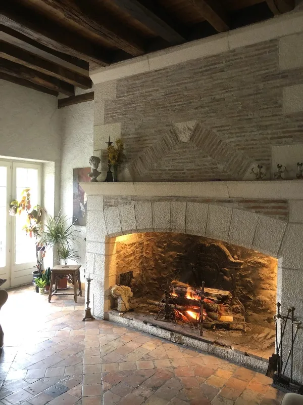 Salon avec trois canapés et grande cheminée en pierre sous charpente ancienne