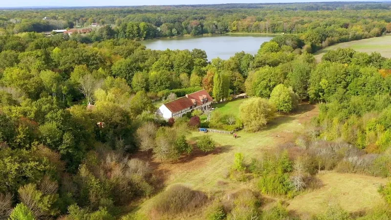 Vue aérienne du domaine de vingt hectares avec la longère à colombages, l'étang et la forêt