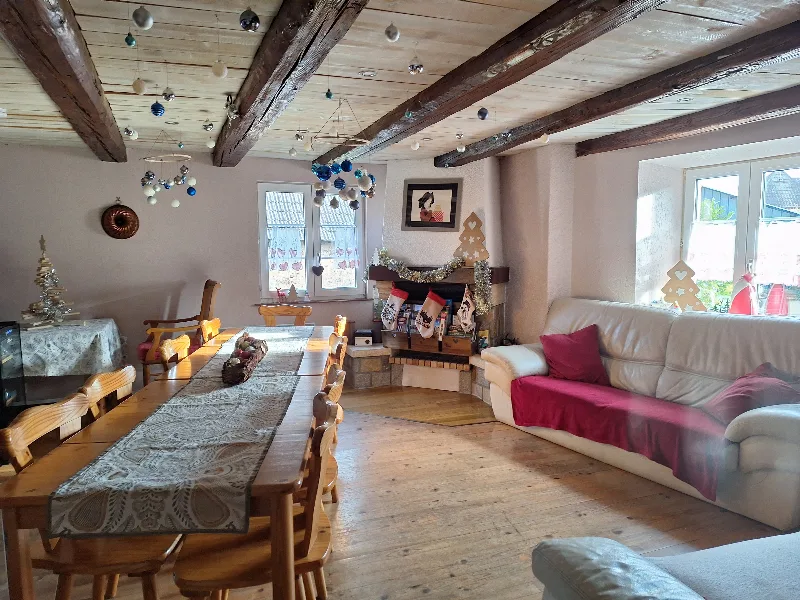 Séjour avec poutres apparentes, cheminée décorée et grande table en bois pour les repas de groupe