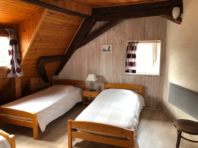 Chambre mansardée avec charpente apparente et deux lits simples sous les combles