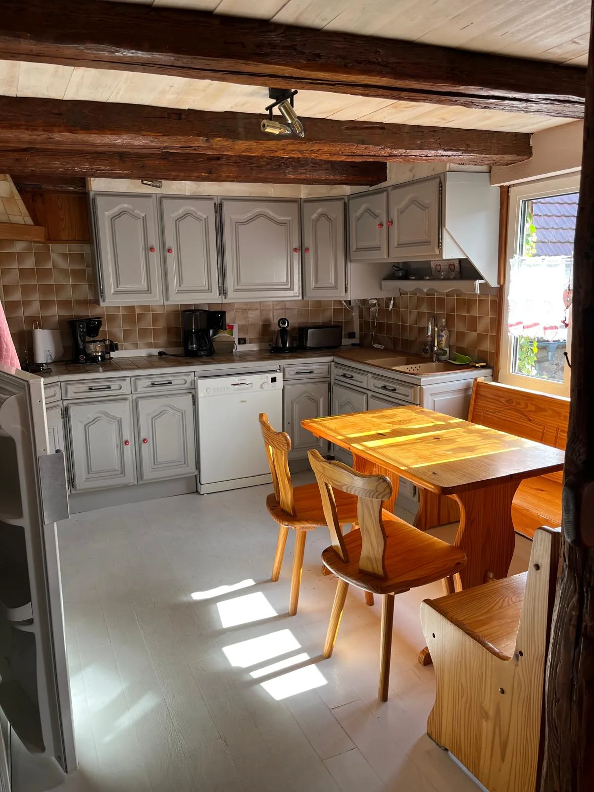 Cuisine équipée avec meubles gris, électroménager complet et table à manger en bois clair