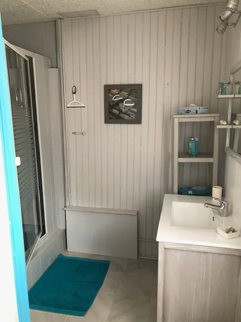 Salle d'eau avec douche à l'italienne, vasque en bois et tapis de bain turquoise