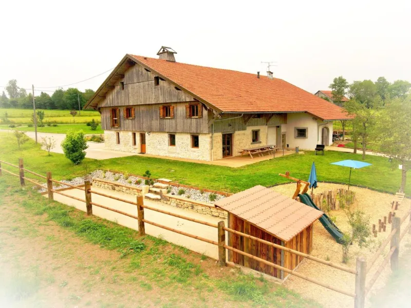 Vue aérienne de la ferme comtoise traditionnelle avec jardin clos et jeux d'enfants