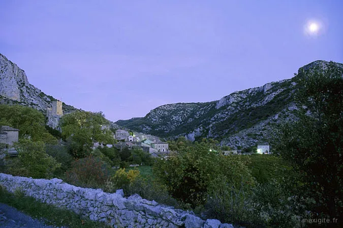 Village blotti dans un cirque de falaises calcaires éclairé au clair de lune