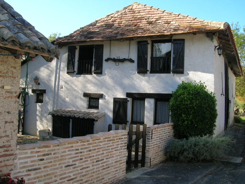 Bâtiment à étage avec volets noirs et mur en pierre apparente, typique du Périgord