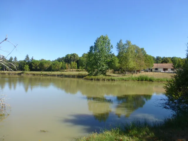 Étang privé du domaine avec la maison visible entre les arbres au loin