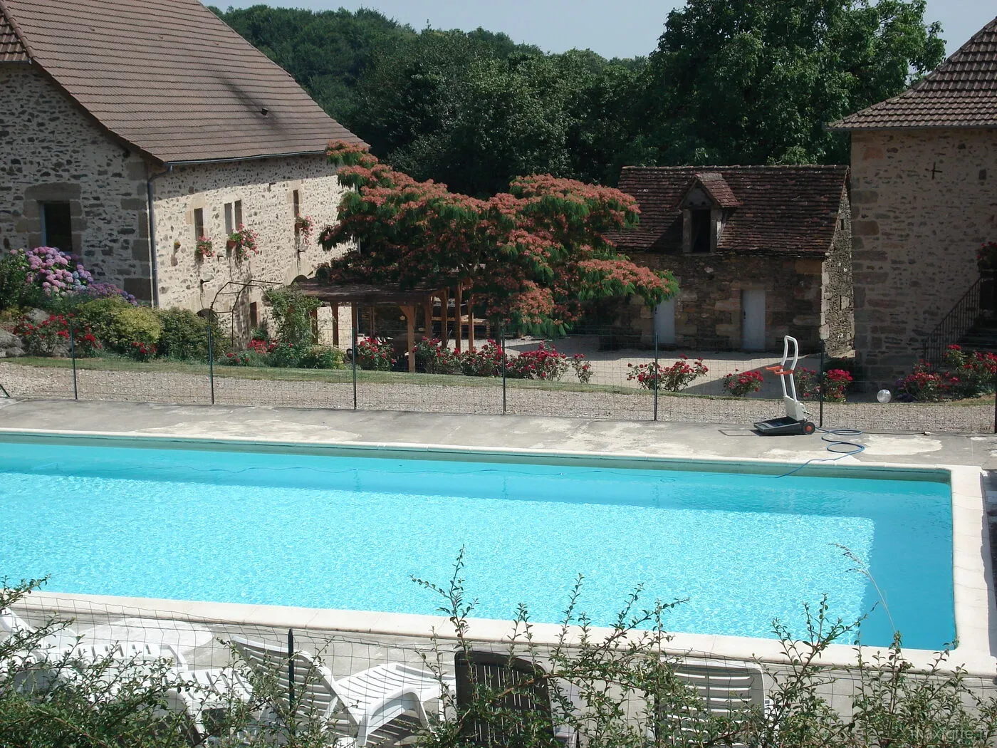 Piscine clôturée avec vue sur les bâtiments en pierre et pergola fleurie
