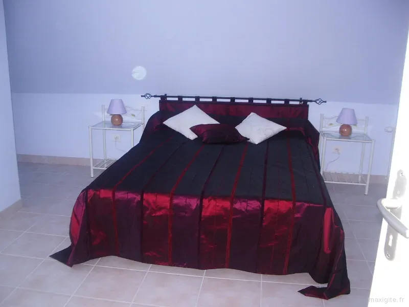 Chambre double avec couvre-lit bordeaux et chevets assortis de part et d'autre du lit