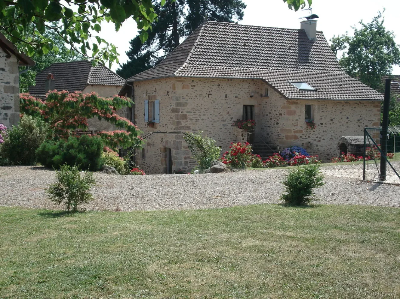 Second bâtiment en pierre du domaine avec volets bleus et massifs de fleurs