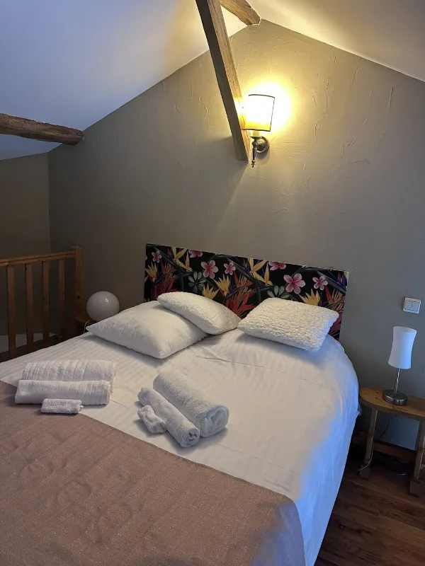 Chambre lumineuse avec tête de lit fleurie, commode en bois et serviettes pliées