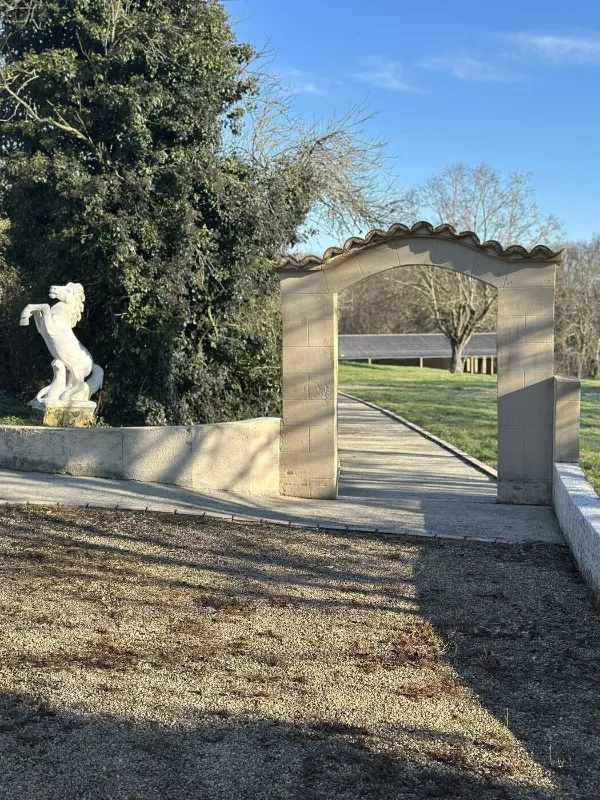 Porche en pierre voûté menant au parc, orné d'une statue de cheval