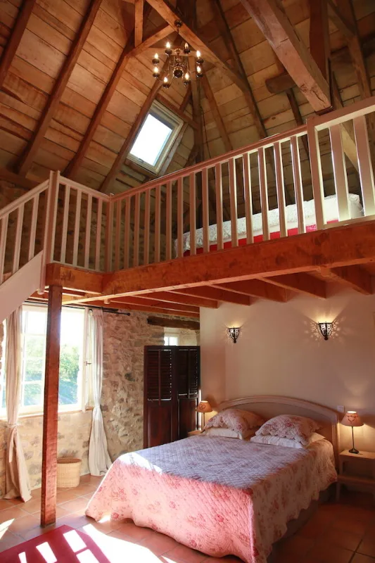 Chambre mezzanine lumineuse avec couvre-lit fleuri et charpente en bois apparente