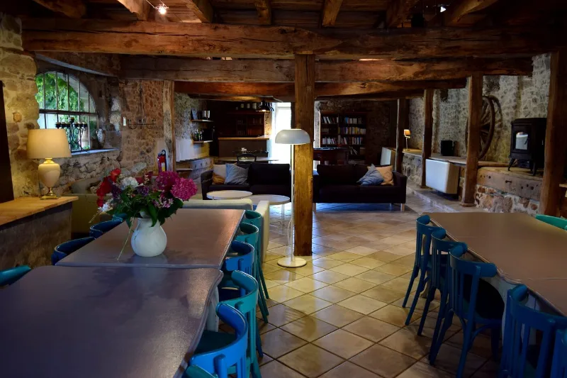 Grand séjour voûté avec poutres apparentes, canapés et longue table conviviale