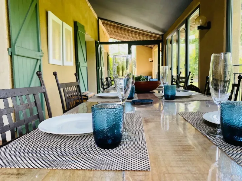 Véranda dressée avec longue table en bois et volets verts pour un repas en groupe