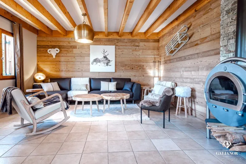 Salon chaleureux avec grand canapé d'angle, poêle à bois rond et poutres apparentes en bois