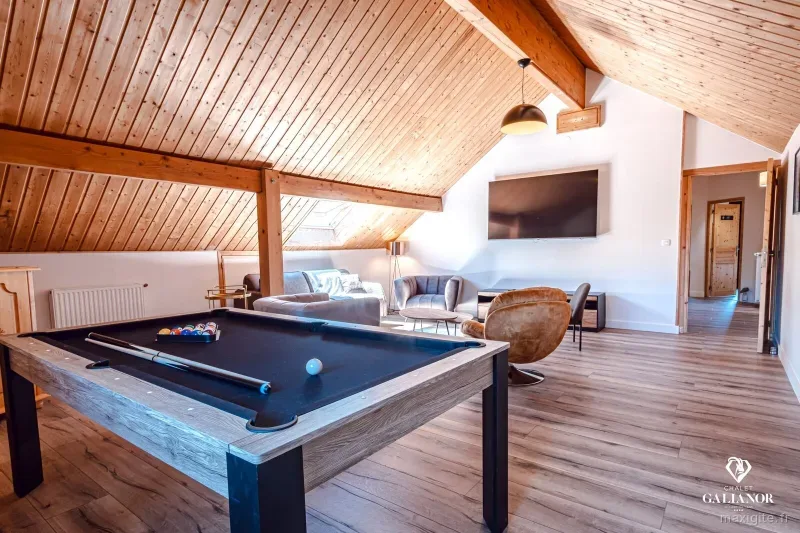 Salle de billard sous combles avec poutres en bois et grand écran TV