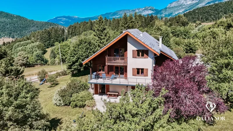 Vue aérienne d'été du chalet en bois avec toit ardoise, entouré de forêt et sommets du Vercors