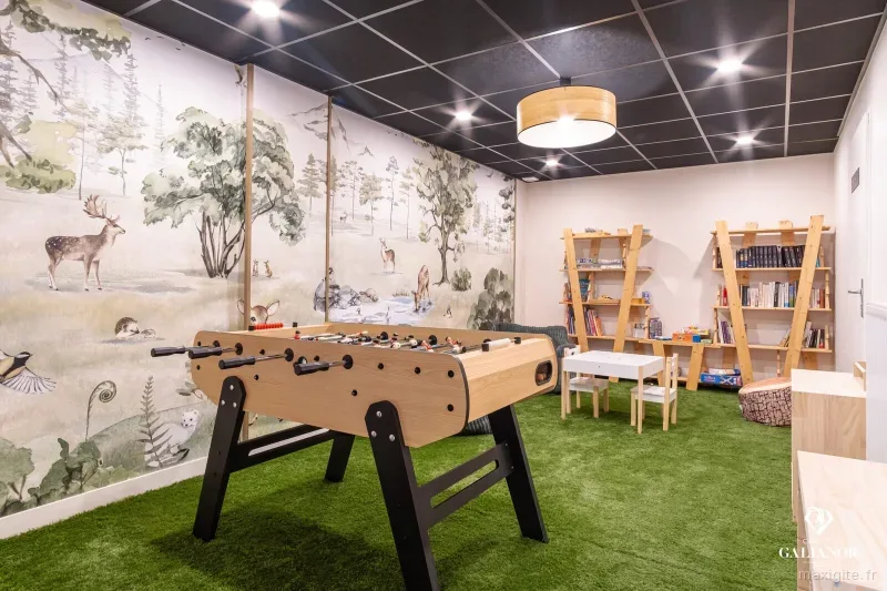 Salle de jeux avec baby-foot, fresque forestière et coin bibliothèque pour enfants