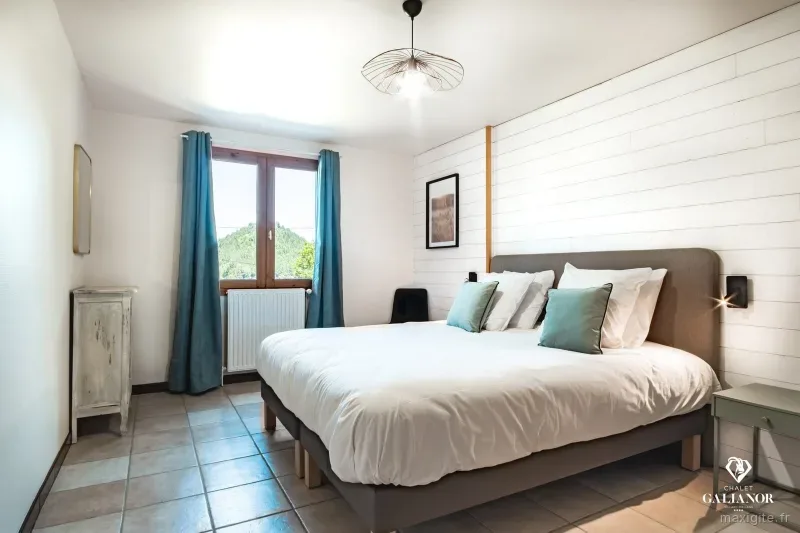 Chambre double lumineuse avec tête de lit capitonnée grise et coussins bleus
