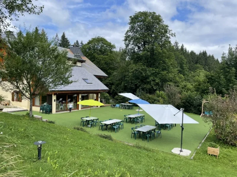 Façade du chalet avec grande terrasse couverte, tables et parasols pour les repas en extérieur
