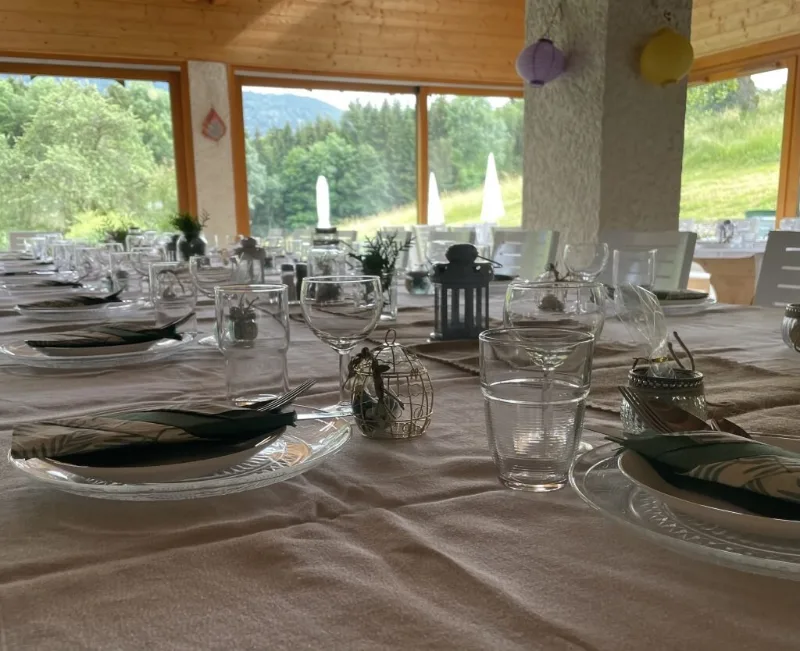 Salle de réception avec tables dressées et grandes baies vitrées ouvertes sur la campagne environnante