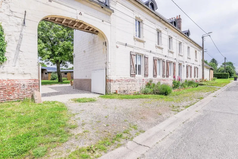 Grand bâtiment en pierre picarde avec porche cintré et volets bleus, façade principale du gîte