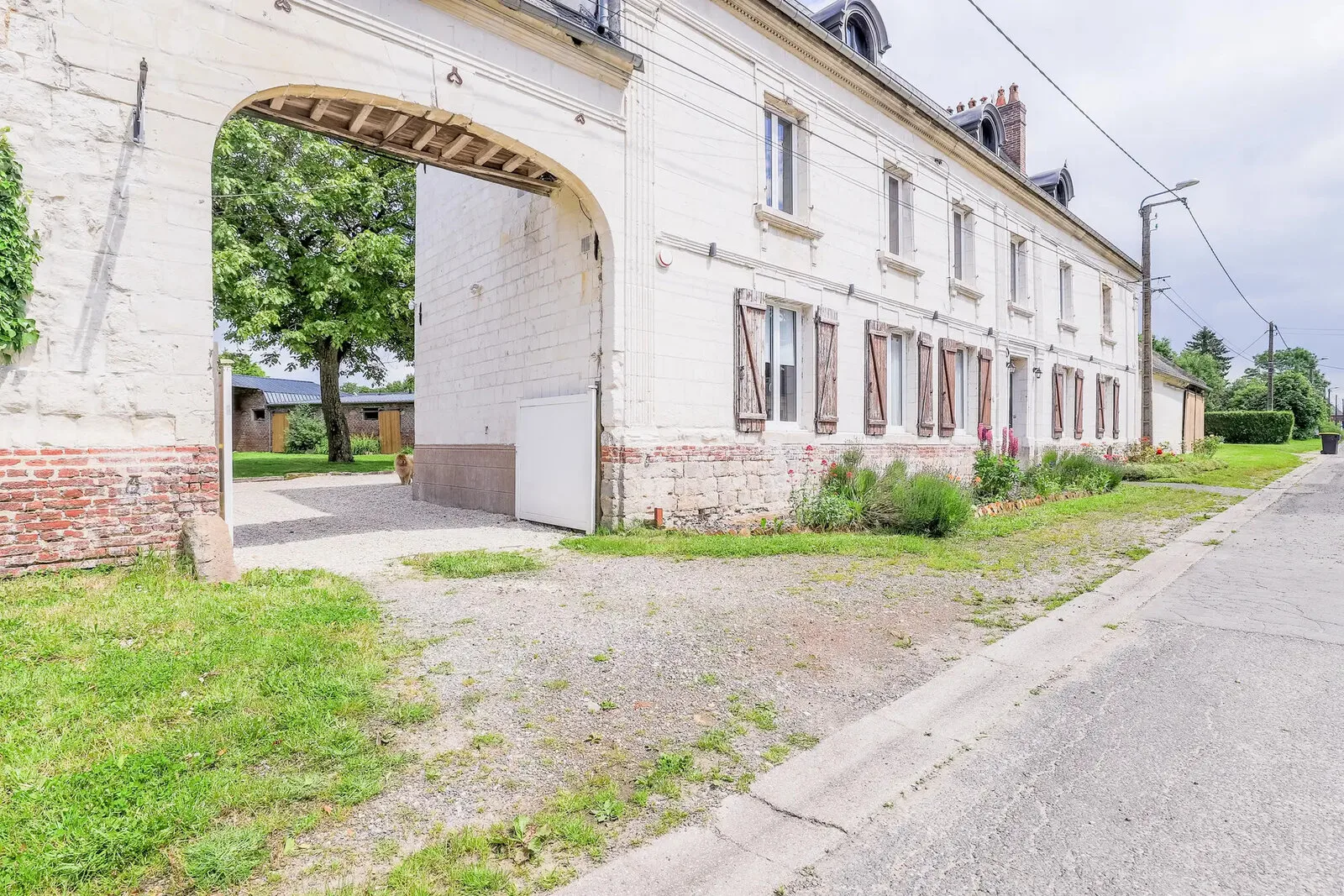 Gîte de groupe La Ferme des Pommés à Pommera — Grand bâtiment en pierre picarde avec porche cintré et volets bleus, façade principale du gîte, capacité 15 personnes