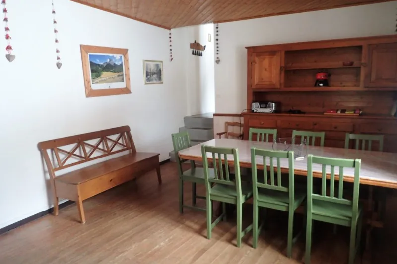 Salle à manger de chalet avec chaises vertes, buffet en pin et photos de montagne