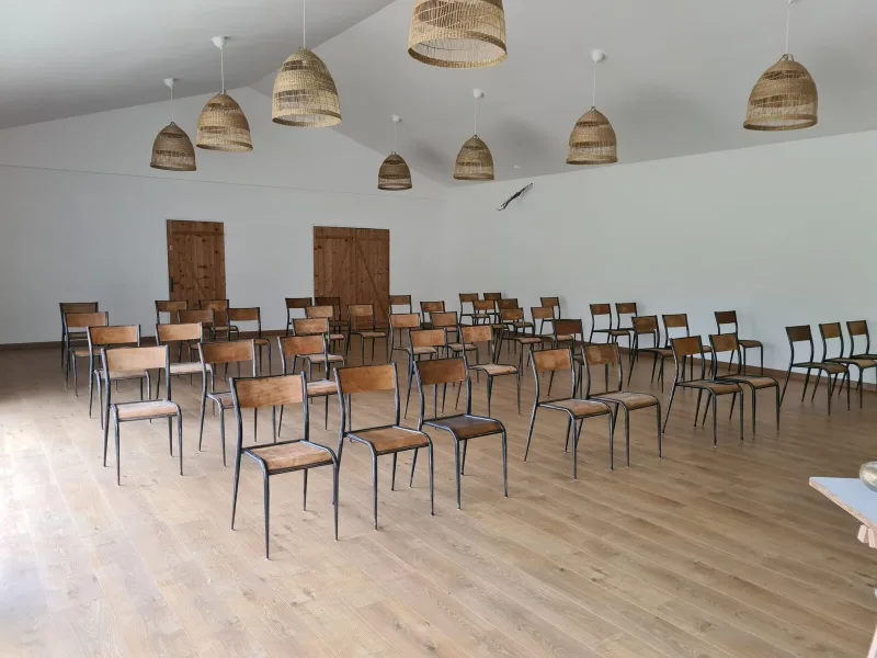 Grande salle de réunion aux poutres apparentes avec chaises en bois disposées pour un atelier collectif