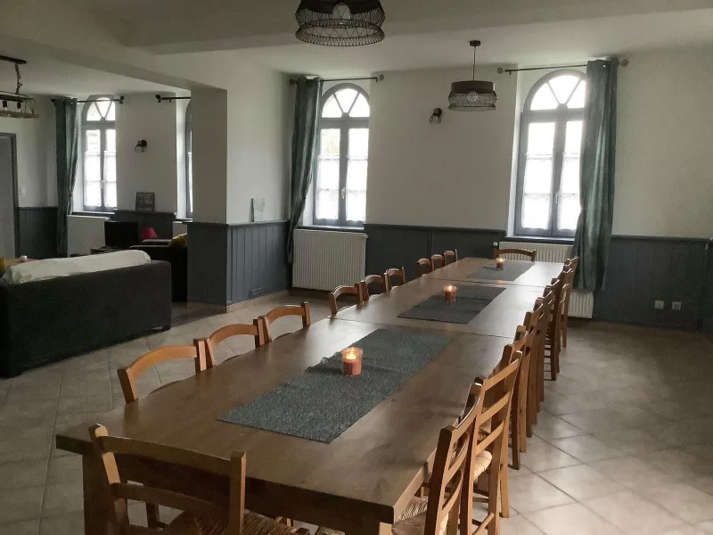 Grand salon avec canapés et longue table en bois dressée pour les repas de groupe