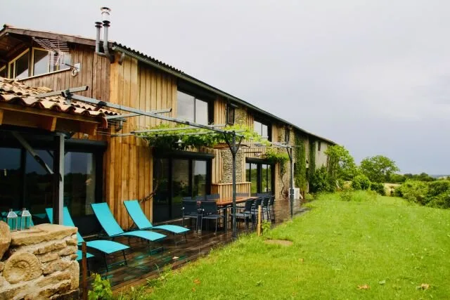 Gîte de groupe Gîte du Logis de Brégion à Sepvret — Façade en bois et pierre du gîte avec terrasse couverte et grande table extérieure, capacité 14 personnes