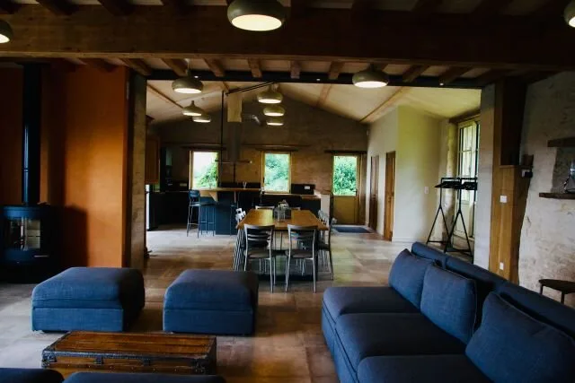 Grand salon ouvert sur la cuisine et la salle à manger, poutres et murs en pierre apparente