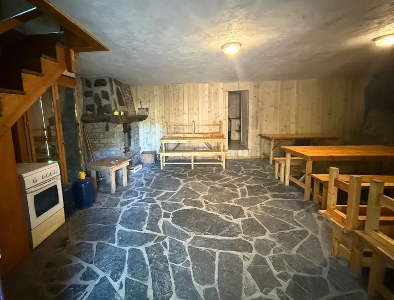 Grande salle rustique avec cheminée en pierre et longues tables en bois pour les repas de groupe