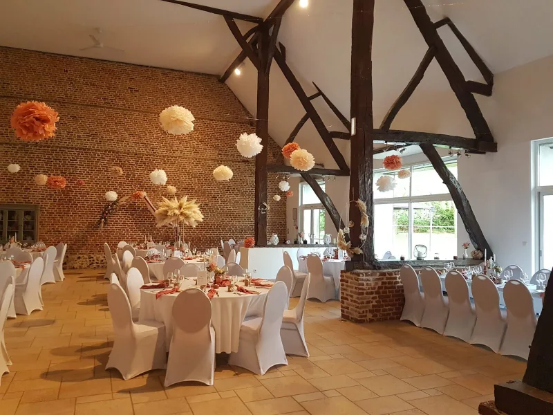 Grande salle de réception aux poutres apparentes avec tables rondes dressées pour un groupe