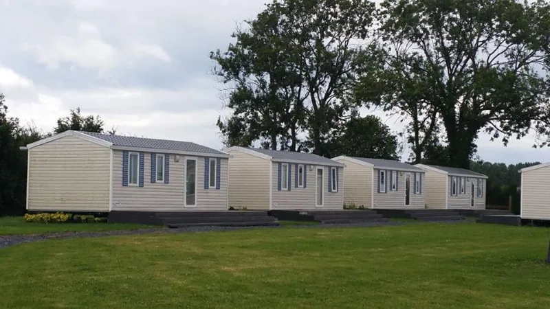 Rangée d'hébergements individuels avec terrasse en bois, pelouse et arbres environnants