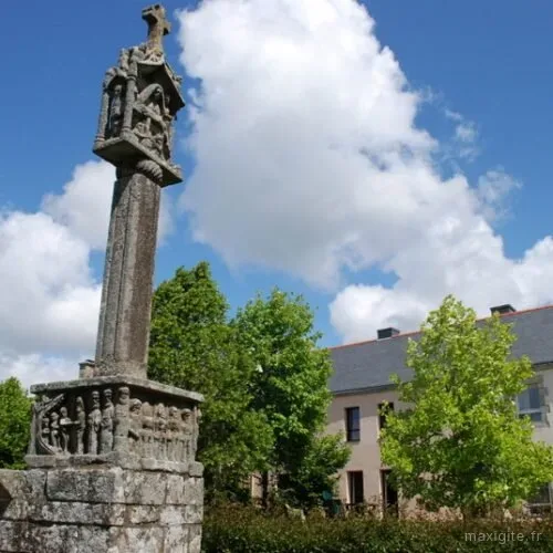 Calvaire en granit devant la longère bretonne, entouré d'arbres et de verdure