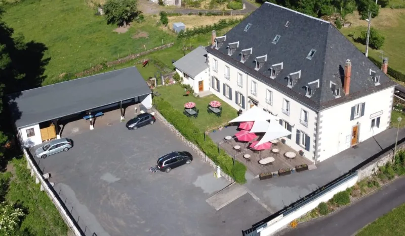 Vue aérienne du corps de ferme auvergnat avec cour, terrasses ombragées et grand parking privé