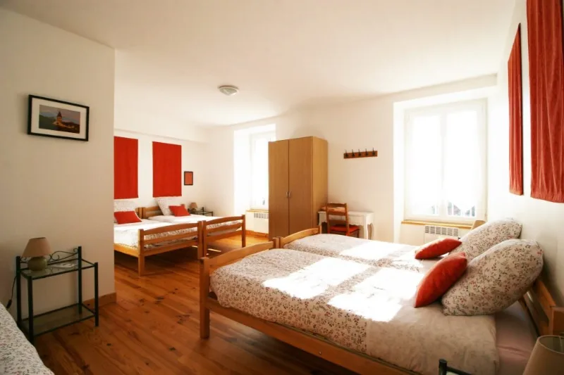 Chambre familiale avec plusieurs lits, tissus rouges et armoire en bois clair